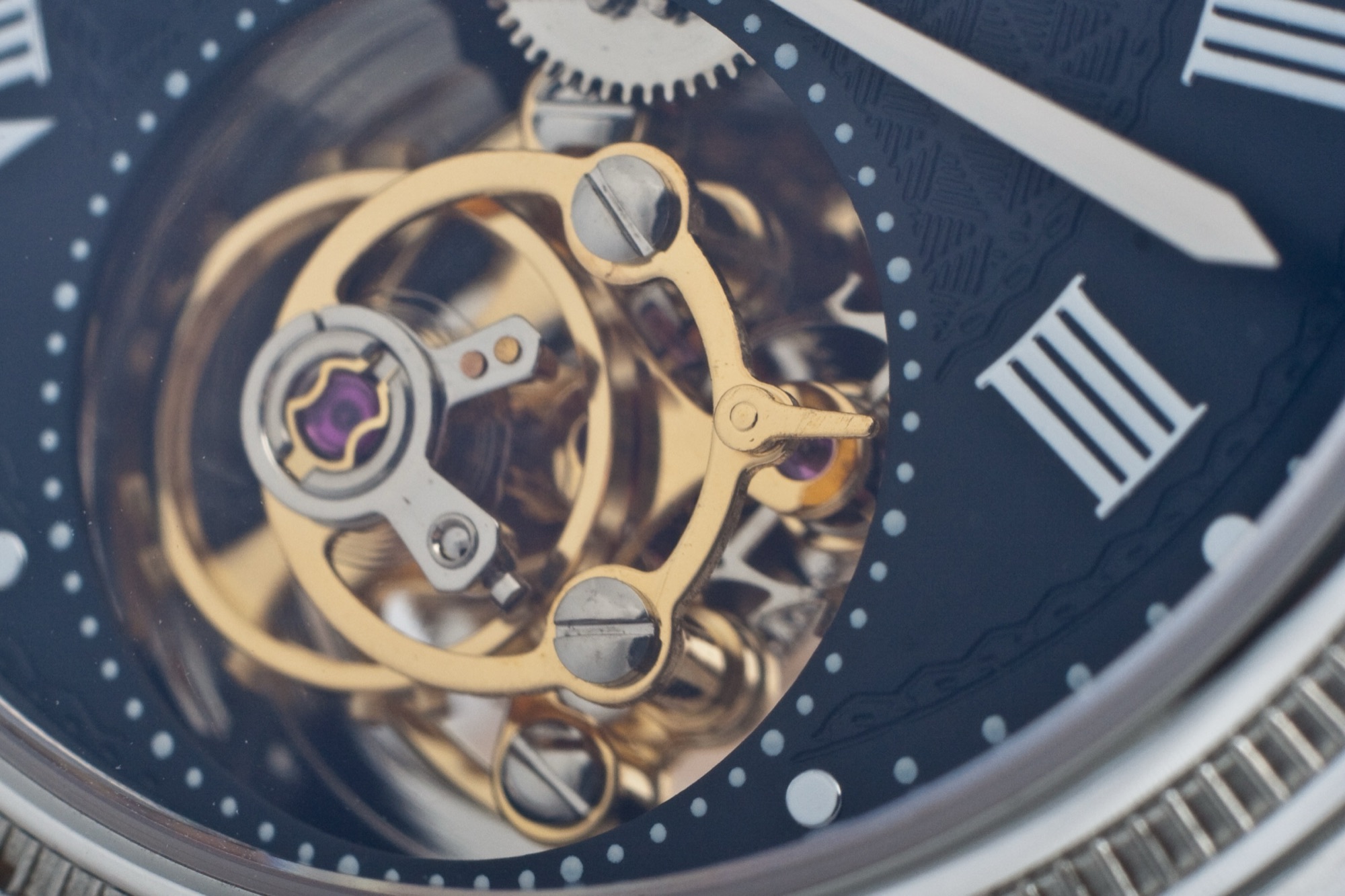 A gold balance wheel beating behind a black dial